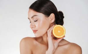 Close up image of charming woman with soft fresh skin holding juicy orange having detox isolated over white background