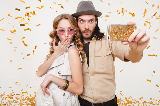 young stylish hipster couple in love making self photo, celebrating disco party, having fun, amazed, exited, funny face, golden confetti, holding phone, trendy apparel, cruise style, white background