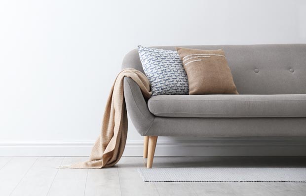 Grey sofa with pillows near white wall in stylish living room in