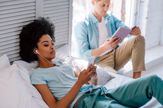 Relaxing woman listening to music on phone while man reading boo