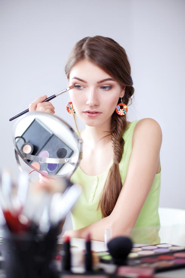 Young beautiful woman making make-up near mirror,sitting at the desk