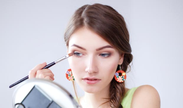 Young beautiful woman making make-up near mirror,sitting at the desk
