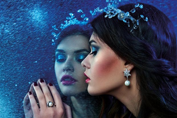 beautiful young girl in pearl jewelry looks at her reflection in