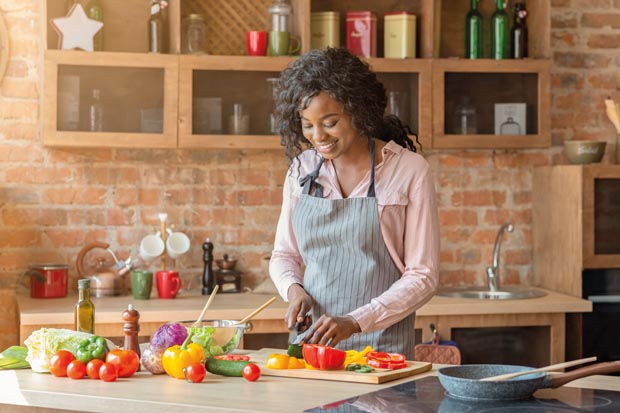 Pretty african american woman preparing healthy veggies salad at kitchen and smiling, copy space