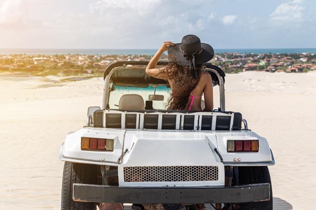 Beautiful happy young woman with buggy ride through the dunes of the coast of Brazil.