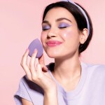 Happy modern young girl hold lilac makeup egg sponge enjoy